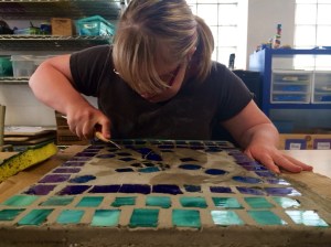 Mariah, an artist with The Arc, works to complete a mosaic stepping stone June 18.