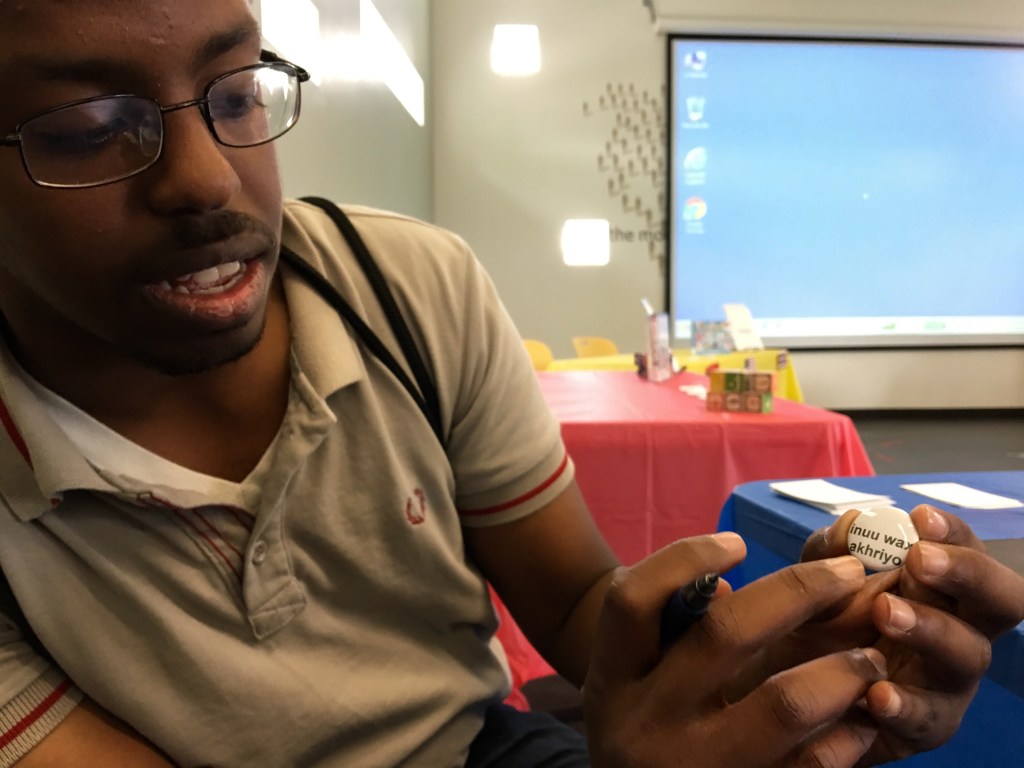 Samir Akal holds a pin that reads "What are you reading?" in Somali.